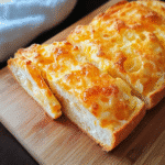 Golden cheese bread sliced on wooden cutting board