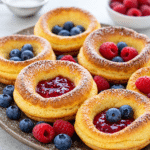 Mini Dutch Baby Pancakes baked in a muffin tin with powdered sugar and fresh berries