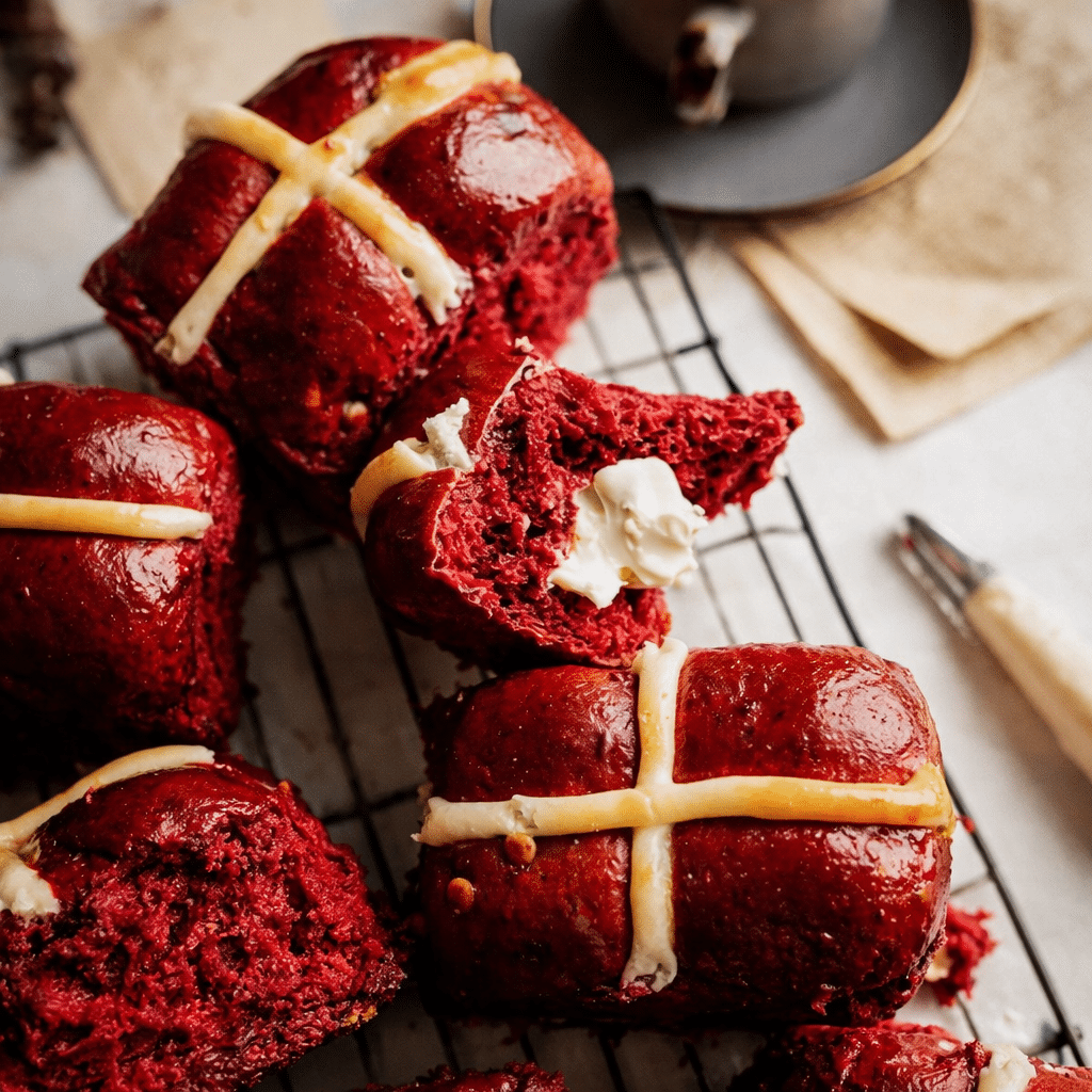 Red velvet hot cross buns with white cross topping and glossy glaze on a baking tray