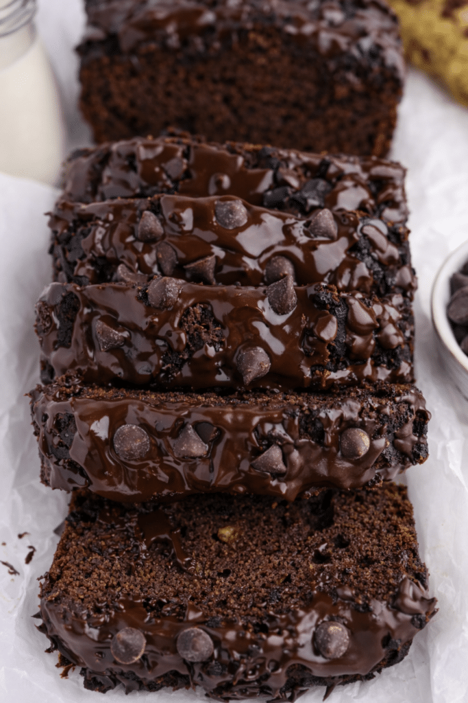 Healthy chocolate banana bread loaf sliced on a wooden board with ripe bananas