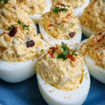 Chicken salad deviled eggs topped with paprika and green onions on a serving platter